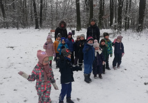 Na zdjęciu widać dzieci oraz panie z grupy na spacerze w parku. W tle drzewa i śnieg.